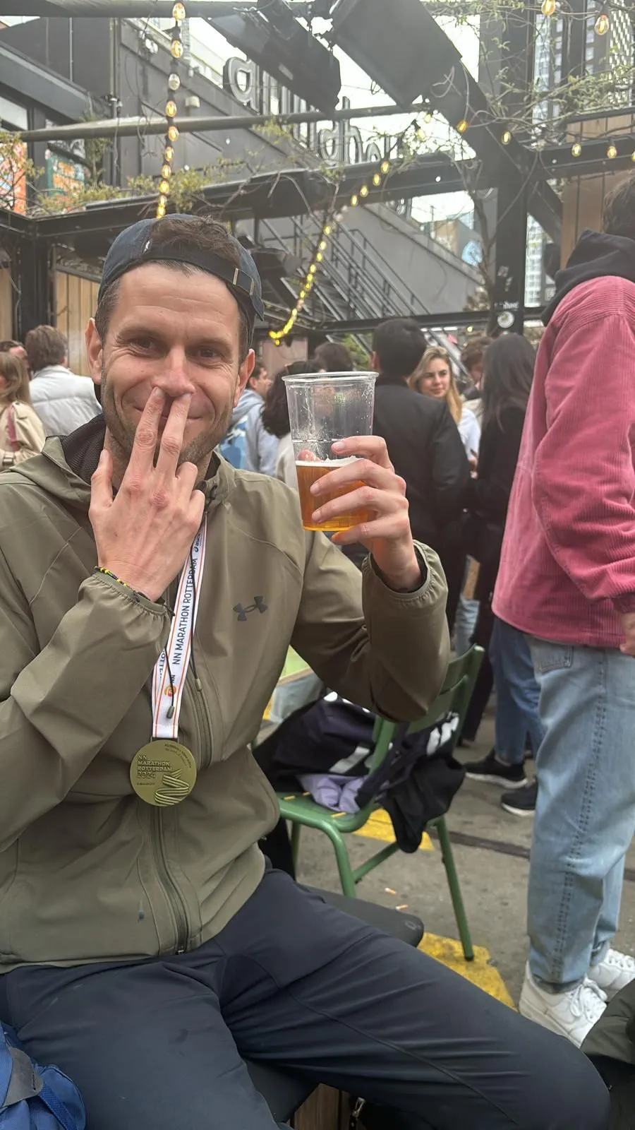 Thomas Sijtsma met medaille, bier en twee vingers in de neus.
